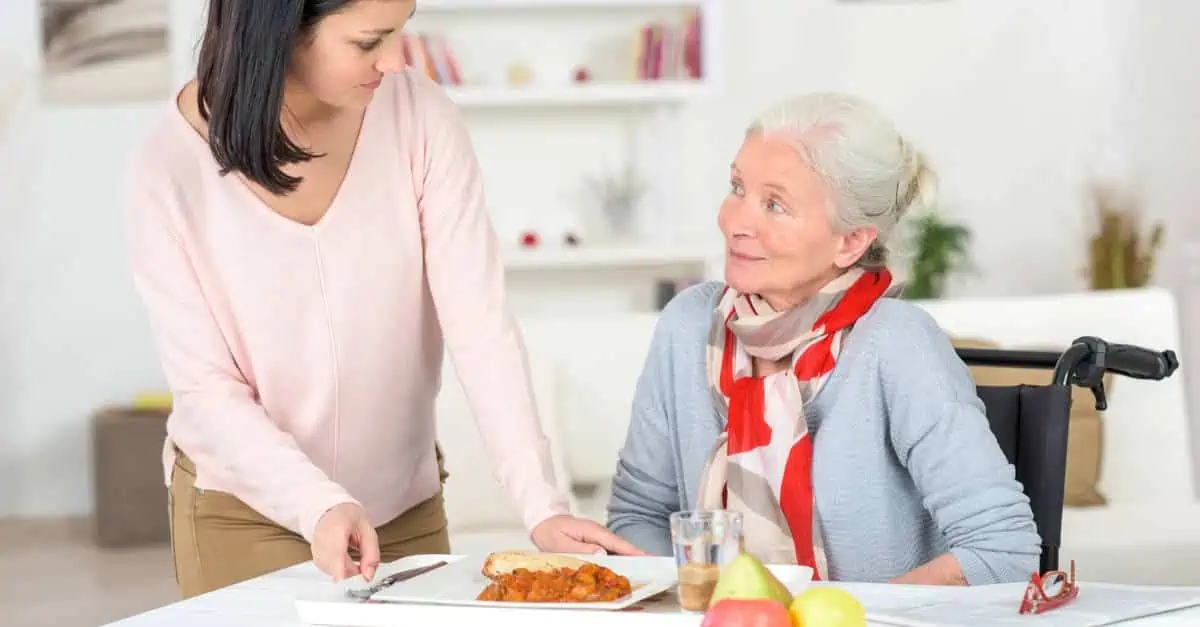 Auxiliaire de vie apportant son repas à une personne agée